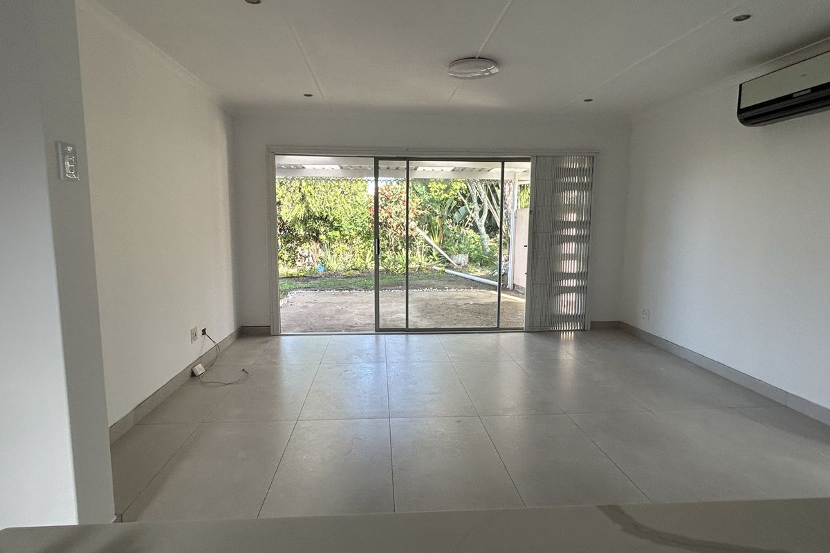 A bright, open-plan living area featuring neutral tiled flooring, recessed lighting, and large sliding glass doors that provide direct access to the rear garden.