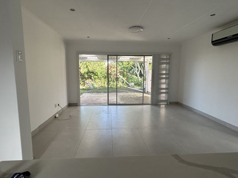 A bright, open-plan living area featuring neutral tiled flooring, recessed lighting, and large sliding glass doors that provide direct access to the rear garden.