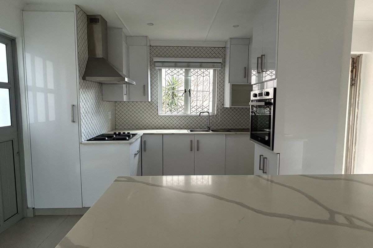 Modern kitchen featuring white cabinetry, stone countertops, built-in oven, gas hob, and a stylish tiled backsplash with ample natural light.