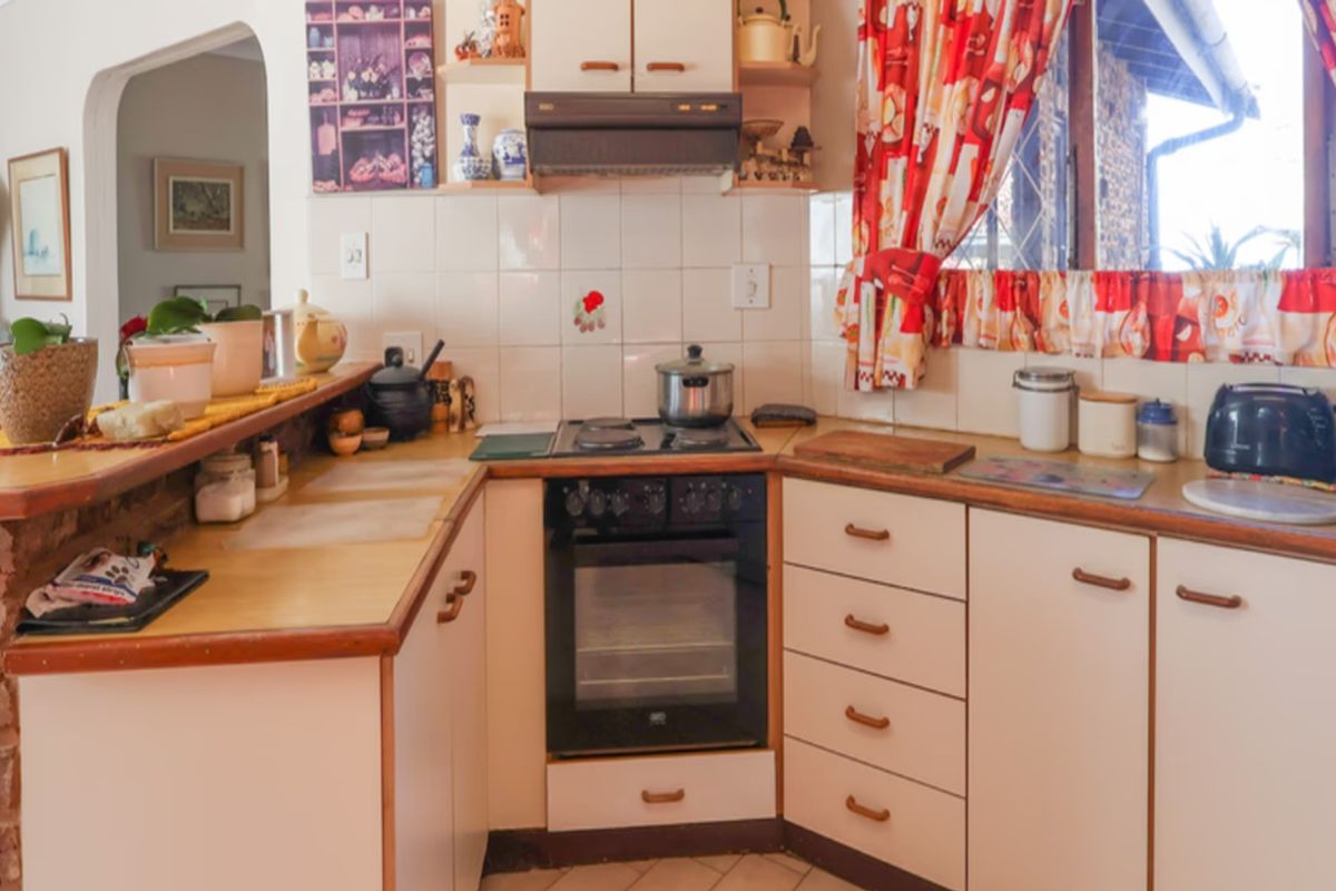 A functional kitchen featuring built-in cabinetry, laminate countertops, an electric oven with hob, and a brick-based breakfast bar, offering a classic, dated aesthetic.