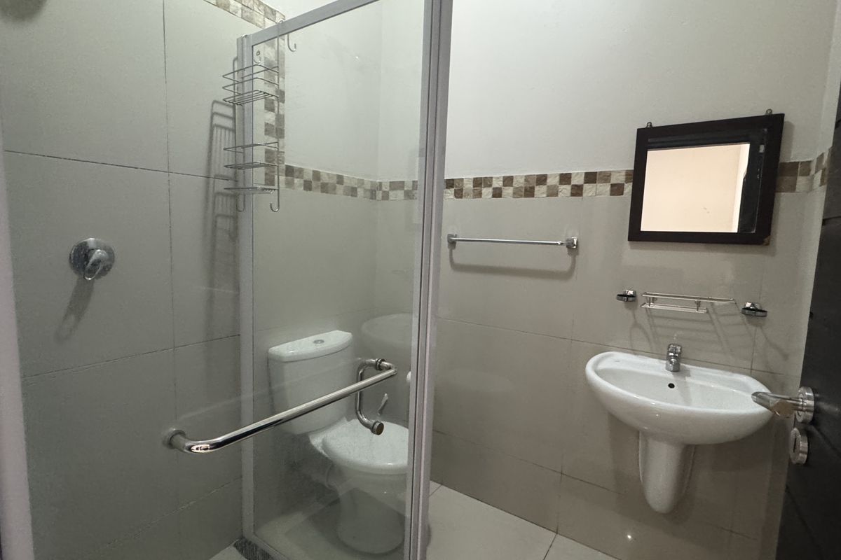 A functional bathroom featuring a glass-enclosed shower, pedestal washbasin, and toilet with neutral wall tiling and chrome fixtures.