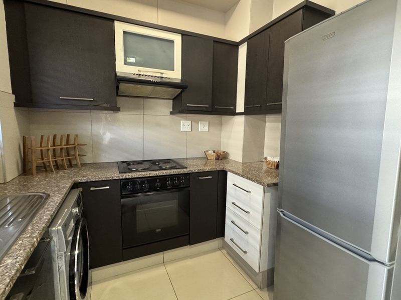 A functional kitchen featuring dark cabinetry, granite countertops, a built-in oven with hob, and an extractor fan, complemented by tiled flooring and backsplash.
