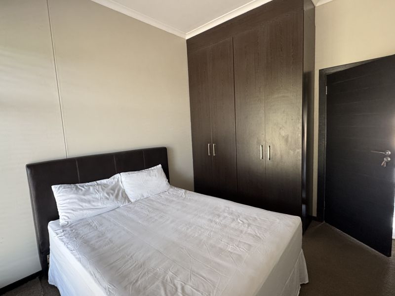 A well-maintained bedroom featuring dark wood built-in cupboards, neutral wall finishes, and carpeted flooring.