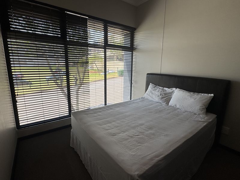 A bedroom featuring large floor-to-ceiling windows with venetian blinds, providing ample natural light and a view of the exterior.