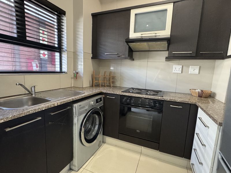 Compact kitchen featuring dark cabinetry, granite countertops, built-in oven with hob, extractor fan, and integrated space for a washing machine.