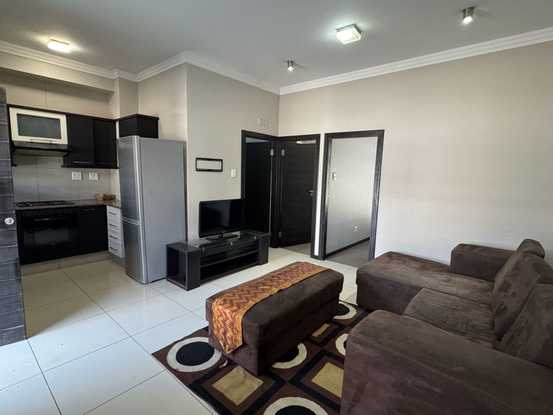 Open-plan living area featuring a modern kitchen with dark cabinetry, granite countertops, and tiled flooring, seamlessly flowing into the lounge space.