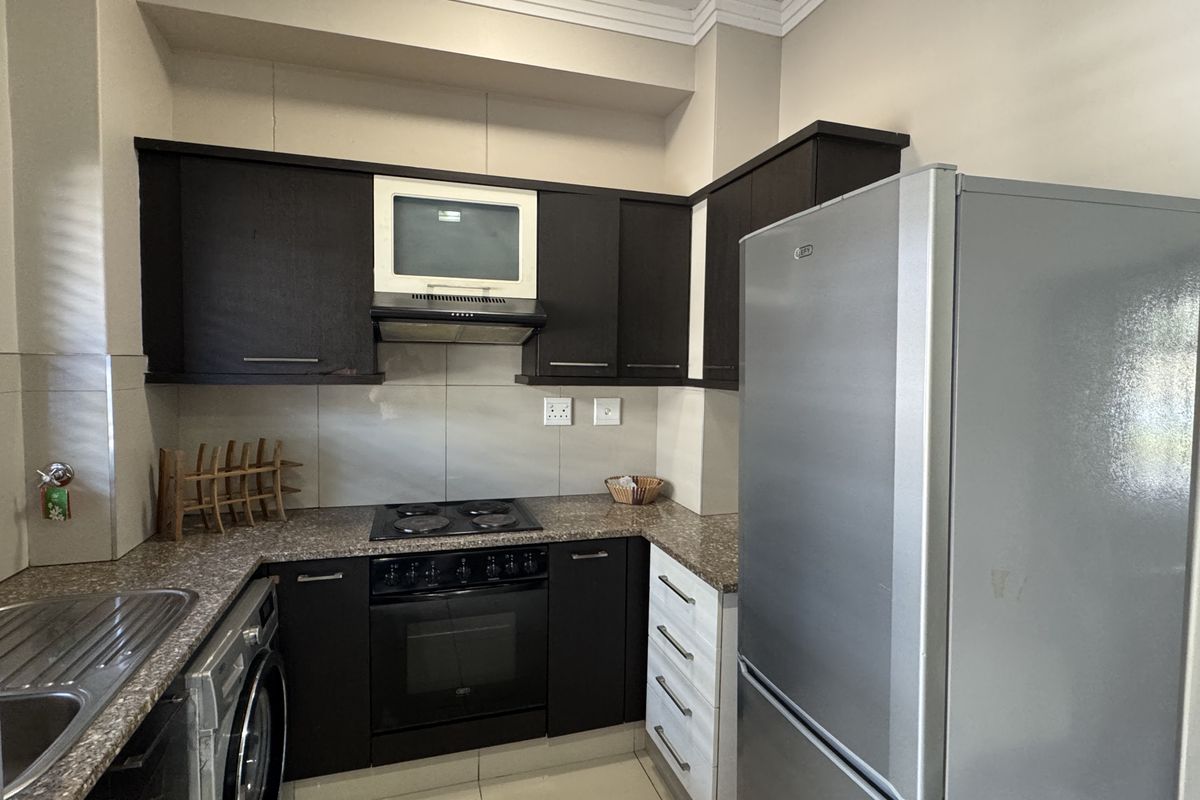 A functional kitchen featuring dark wood cabinetry, granite countertops, built-in oven with hob, extractor fan, and a stainless steel sink.