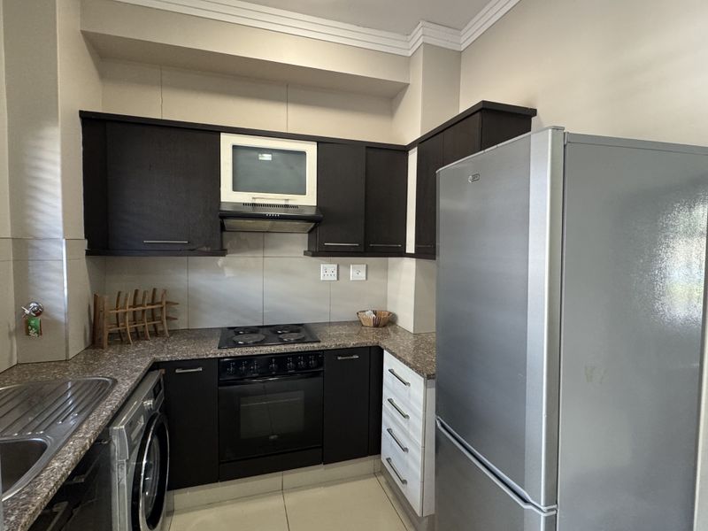 A functional kitchen featuring dark wood cabinetry, granite countertops, built-in oven with hob, extractor fan, and a stainless steel sink.