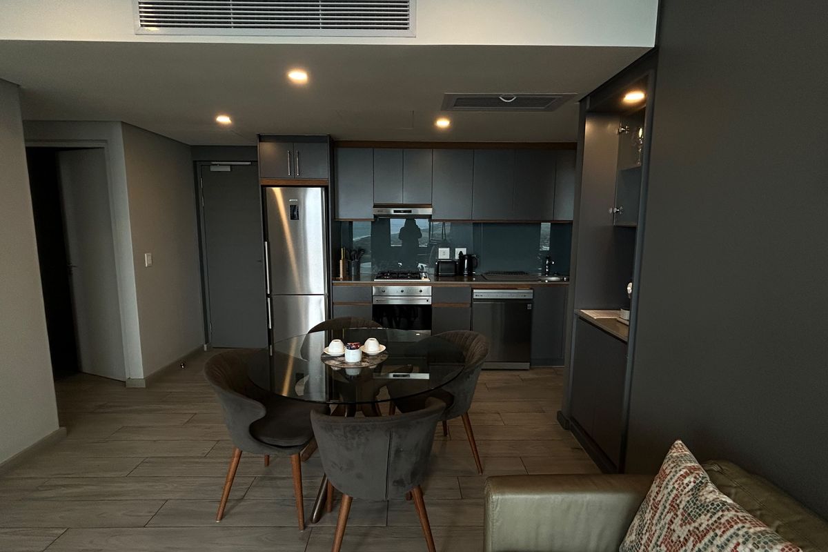 Modern open-plan living area featuring a sleek kitchen with integrated appliances, recessed lighting, ducted air conditioning, and contemporary tiled flooring.