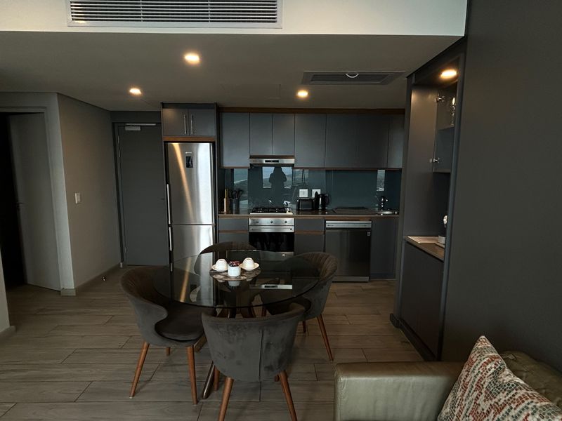 Modern open-plan living area featuring a sleek kitchen with integrated appliances, recessed lighting, ducted air conditioning, and contemporary tiled flooring.