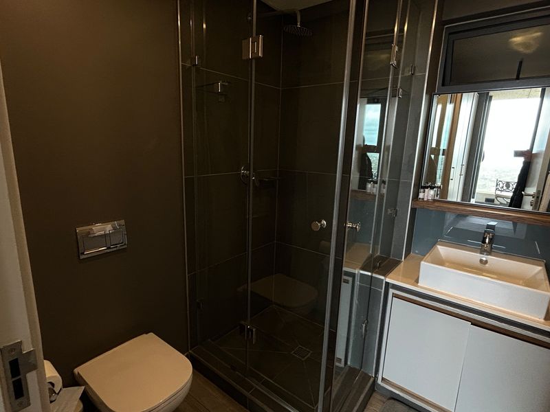 Modern bathroom featuring a glass-enclosed shower, wall-mounted toilet, and a sleek vanity with a vessel sink.