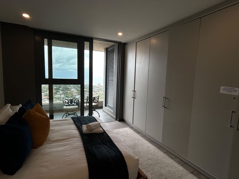 Modern bedroom featuring extensive built-in cupboards, recessed lighting, and a sliding glass door leading to a private balcony with scenic views.