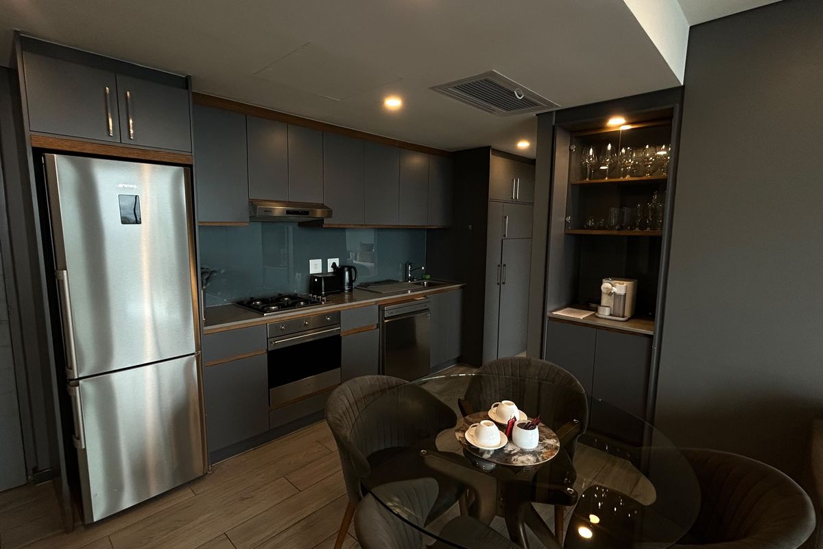 Modern open-plan kitchen featuring dark grey cabinetry, integrated appliances, gas hob, and sleek glass splashback, seamlessly flowing into the dining area.