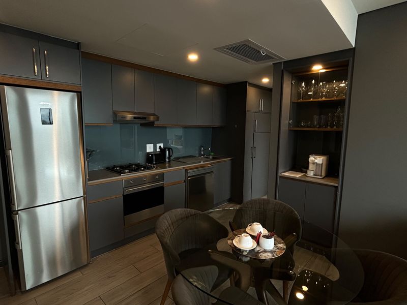 Modern open-plan kitchen featuring dark grey cabinetry, integrated appliances, gas hob, and sleek glass splashback, seamlessly flowing into the dining area.