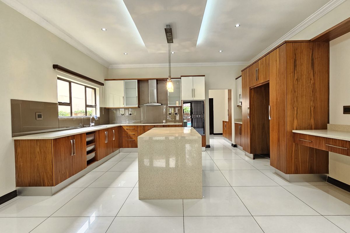 Modern, spacious kitchen featuring high-end wood cabinetry, a large central stone island, sleek tiled flooring, and integrated lighting throughout.