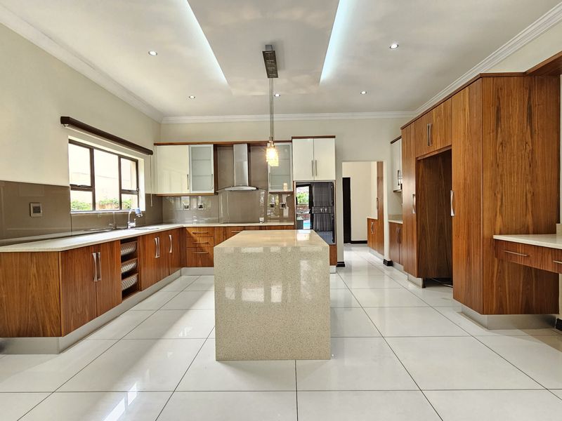 Modern, spacious kitchen featuring high-end wood cabinetry, a large central stone island, sleek tiled flooring, and integrated lighting throughout.