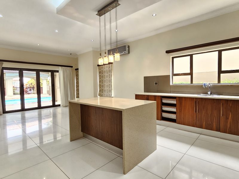 Spacious open-plan kitchen and living area featuring modern wooden cabinetry, stone countertops, a central island, and large sliding doors leading to the pool area.