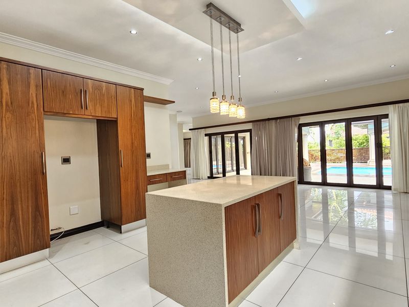 Spacious open-plan kitchen and living area featuring modern wood cabinetry, a central stone island, tiled floors, and large sliding doors opening to the pool area.