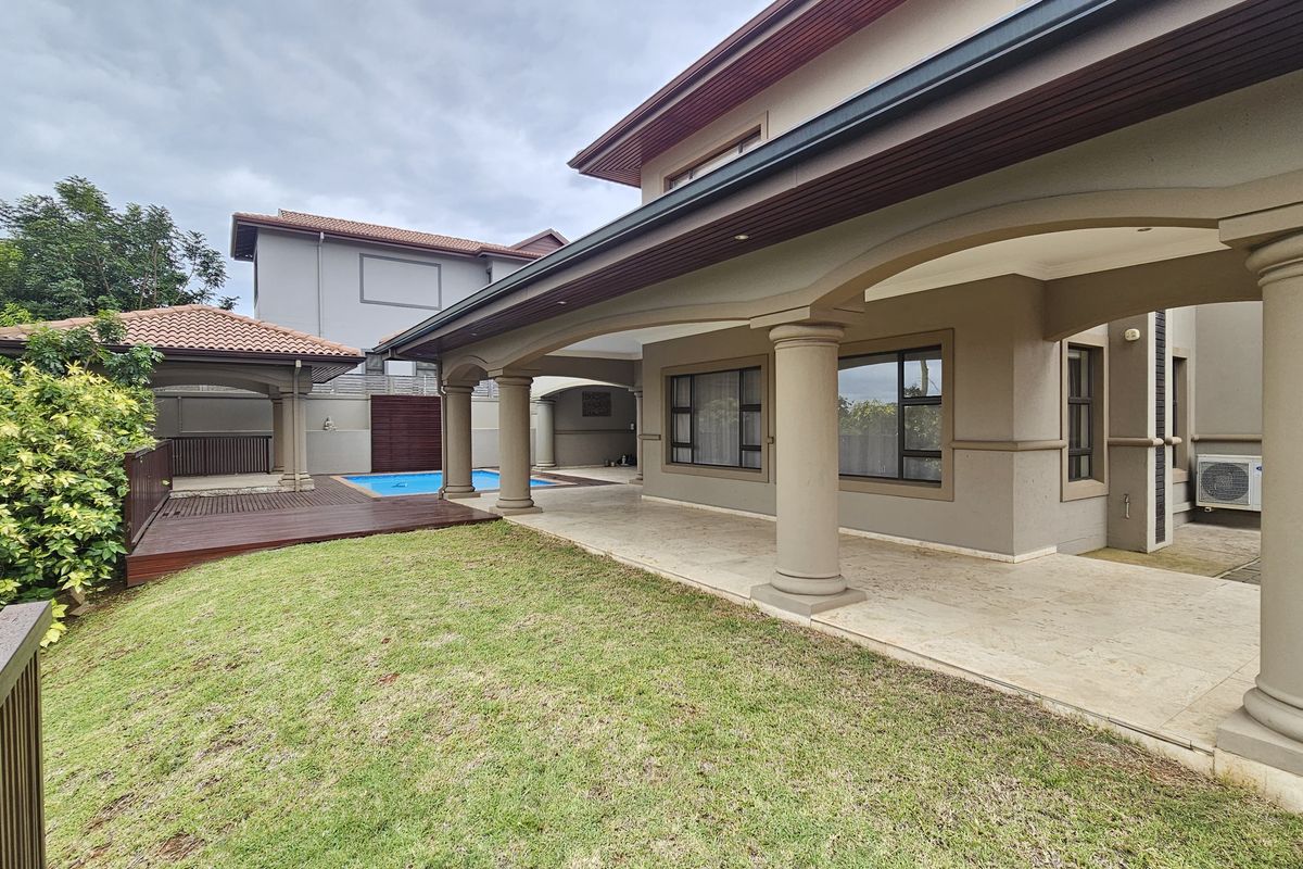 Spacious covered patio overlooking a well-maintained garden, wooden deck, and swimming pool area, perfect for outdoor entertaining.