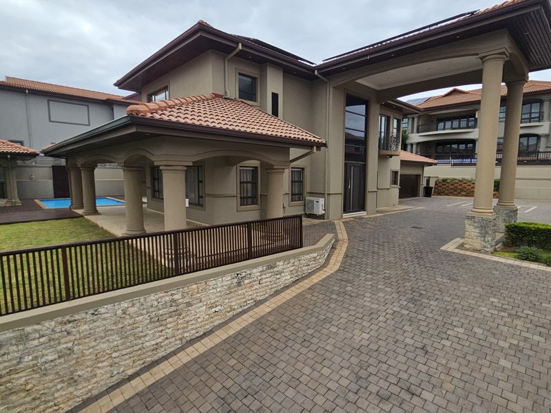 A grand multi-story residence featuring a paved driveway, stone-clad retaining walls, covered entrance with columns, and a private swimming pool area.