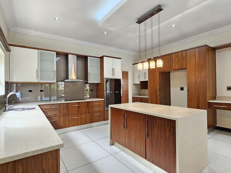 Modern kitchen featuring high-end wood cabinetry, stone countertops, a central island, built-in appliances, and sleek tiled flooring with recessed and pendant lighting.