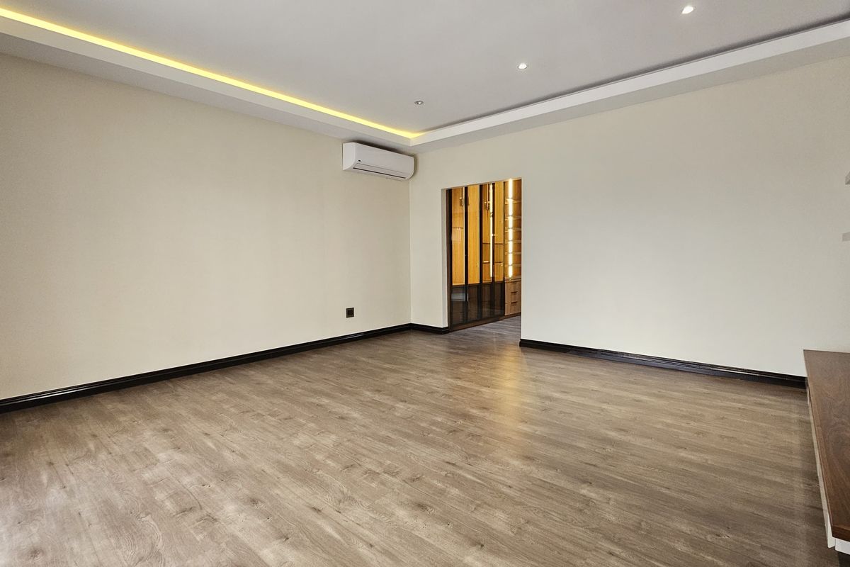 Spacious bedroom featuring modern laminate flooring, recessed cove lighting, and a wall-mounted air conditioning unit, leading into a walk-in closet area.