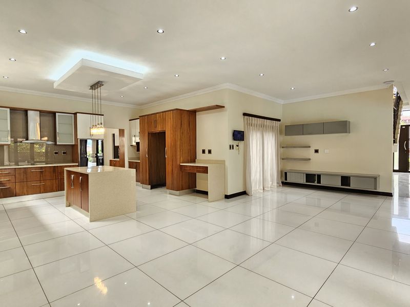 Spacious open-plan kitchen and living area featuring modern wood-finish cabinetry, a central island, stone countertops, and sleek tiled flooring throughout.