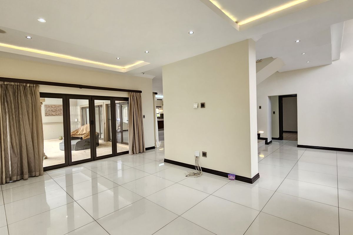 Spacious, light-filled living area featuring polished tile flooring, recessed ceiling lighting, and large sliding glass doors leading to an outdoor space.