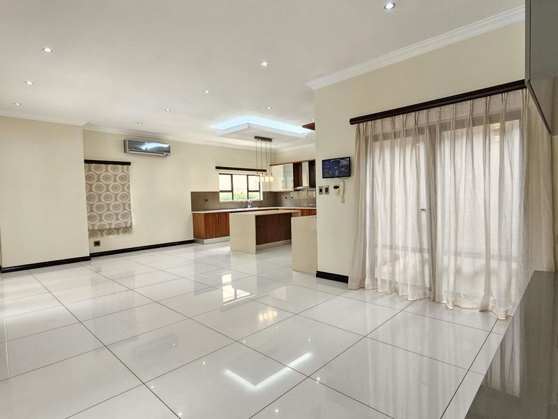Spacious open-plan living and kitchen area featuring polished porcelain tiles, modern cabinetry, a central island, and abundant natural light through sliding glass doors.