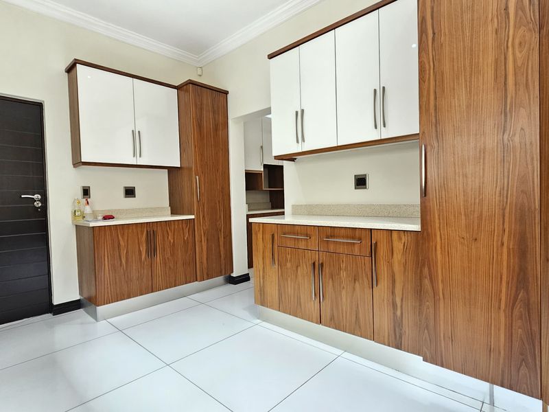 Modern kitchen featuring high-gloss white and wood-grain cabinetry, stone countertops, and large format floor tiles, offering a clean and contemporary aesthetic.