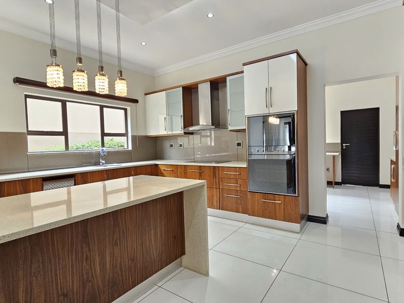 Modern kitchen featuring high-end wood-finish cabinetry, quartz countertops, a central island, and integrated appliances, complemented by sleek tiled flooring and recessed lighting.