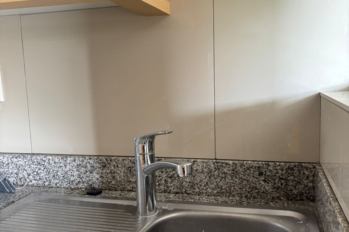 A functional kitchen sink area featuring a stainless steel basin, chrome mixer tap, granite countertop, and neutral tiled splashback.