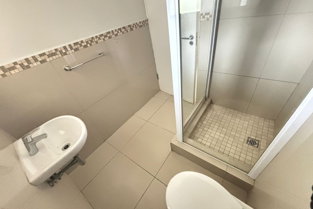 A functional bathroom featuring a shower enclosure, bidet, and toilet with neutral wall and floor tiling.