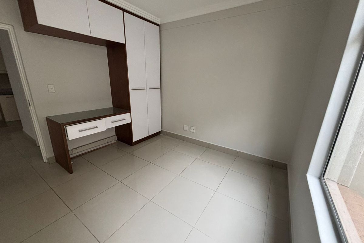 A bright, empty bedroom featuring neutral tiled flooring, built-in cabinetry with an integrated desk, and clean finishes throughout.