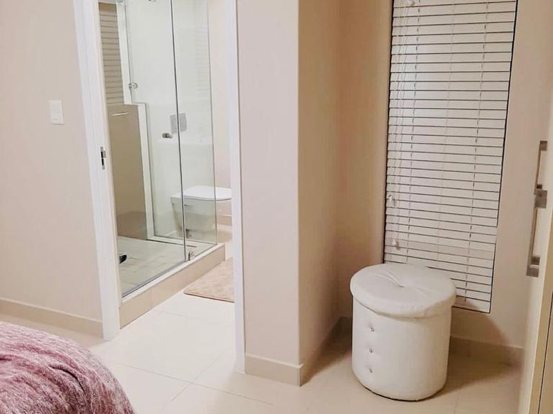 A well-maintained bedroom featuring tiled flooring, venetian blinds, and an integrated en-suite bathroom with a modern glass shower enclosure.