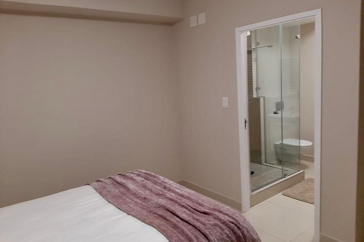 A well-maintained bedroom featuring neutral wall tones, tiled flooring, and direct access to a private en-suite bathroom with a glass-enclosed shower.