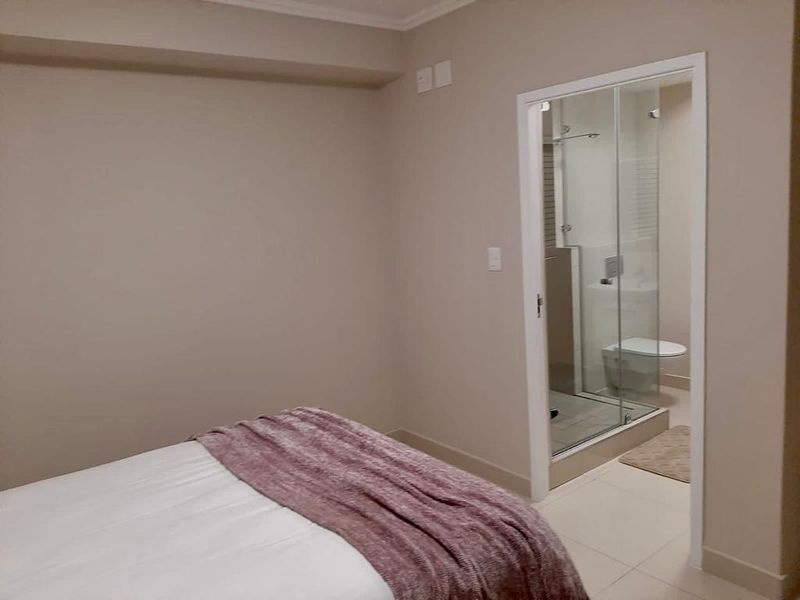 A well-maintained bedroom featuring neutral wall tones, tiled flooring, and direct access to a private en-suite bathroom with a glass-enclosed shower.