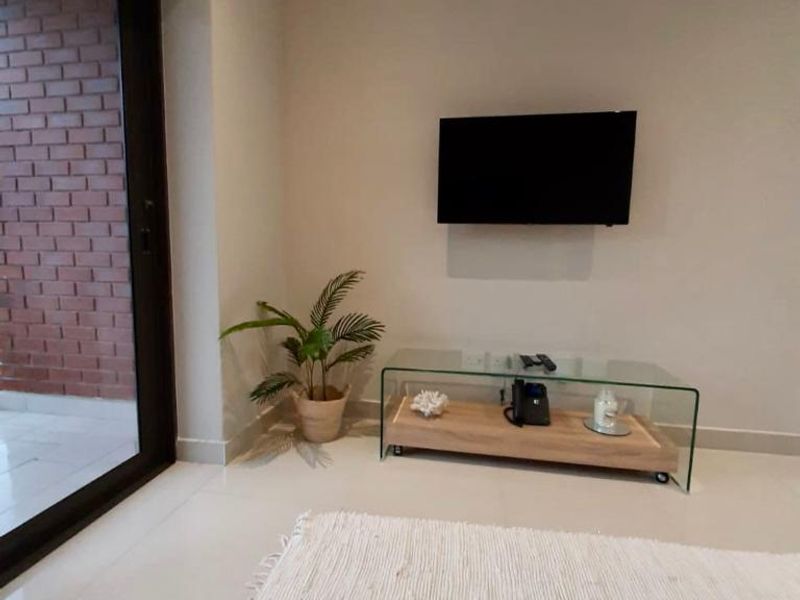 A bright living area featuring neutral tiled flooring, a wall-mounted television, and a large sliding glass door leading to an outdoor space.