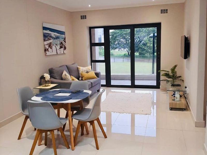 A bright open-plan living and dining area featuring modern porcelain floor tiles, recessed downlights, and large sliding glass doors leading to a balcony.