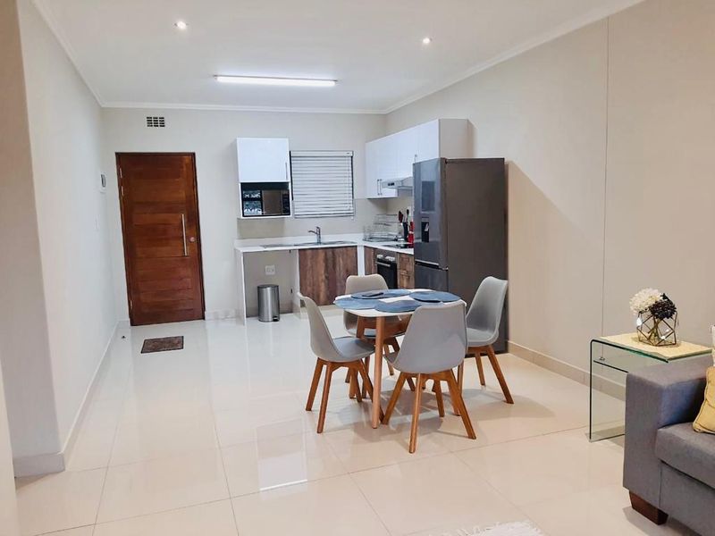 Modern open-plan living area featuring a compact kitchen with built-in cabinetry, tiled flooring, and recessed lighting, seamlessly flowing into the dining space.