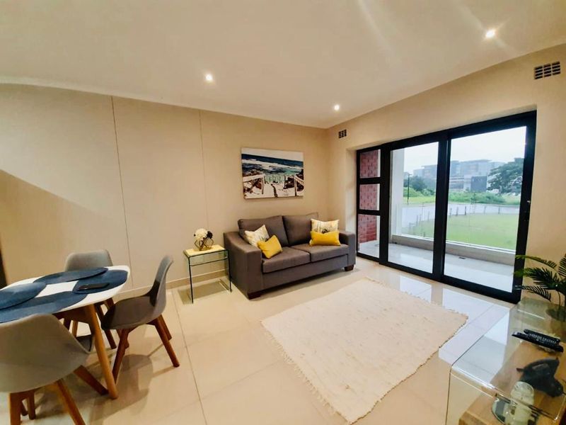 Modern open-plan living area featuring neutral tiled flooring, recessed downlighting, and large sliding glass doors providing access to an outdoor space.