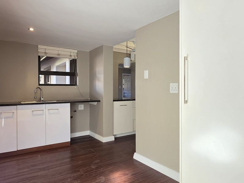 A clean, modern kitchen area featuring white built-in cabinetry, dark laminate flooring, and recessed lighting, offering a functional and neutral space.