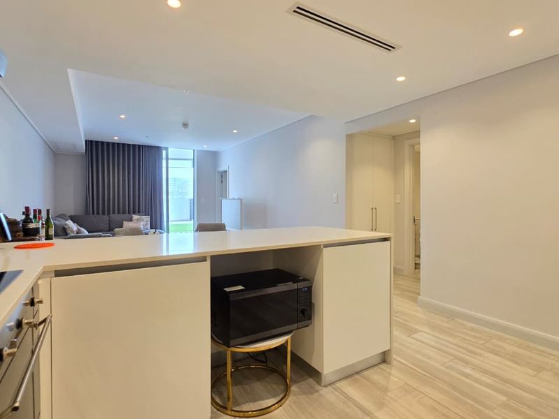 Modern open-plan kitchen and living area featuring sleek cabinetry, stone countertops, integrated appliances, recessed lighting, and neutral tiled flooring throughout.