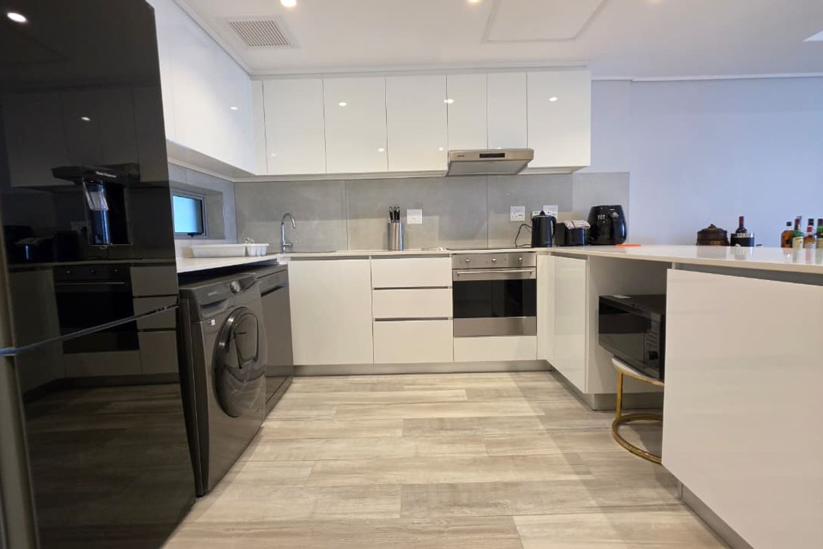 Modern kitchen featuring sleek white cabinetry, stone countertops, integrated appliances, and durable wood-look tile flooring in an open-plan layout.