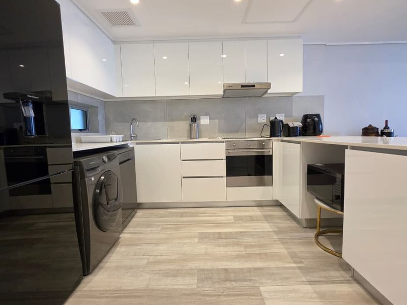 Modern kitchen featuring sleek white cabinetry, stone countertops, integrated appliances, and durable wood-look tile flooring in an open-plan layout.