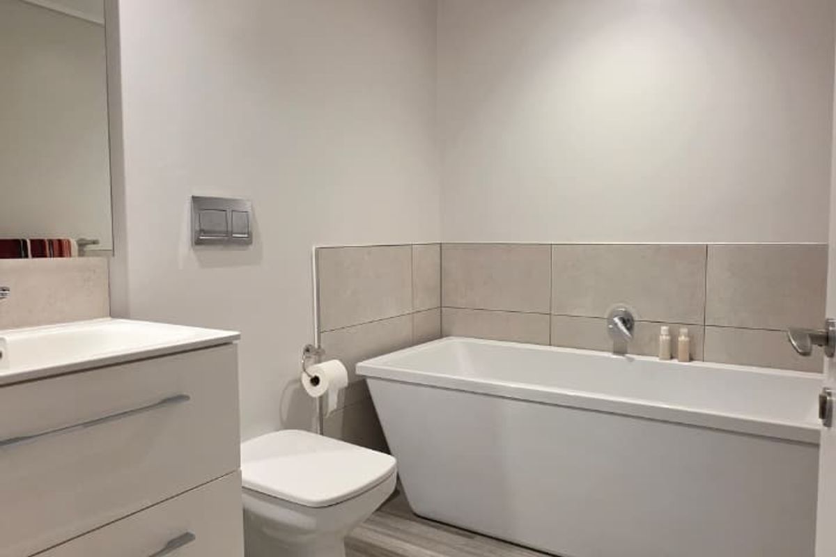 Modern bathroom featuring a sleek freestanding bathtub, wall-mounted toilet, vanity cabinet with integrated sink, and contemporary tiled flooring.