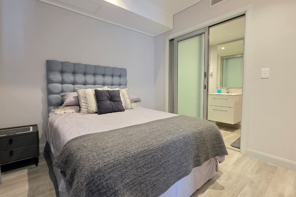 A well-maintained bedroom featuring modern laminate flooring, recessed lighting, and direct access to an en-suite bathroom through a sliding glass door.