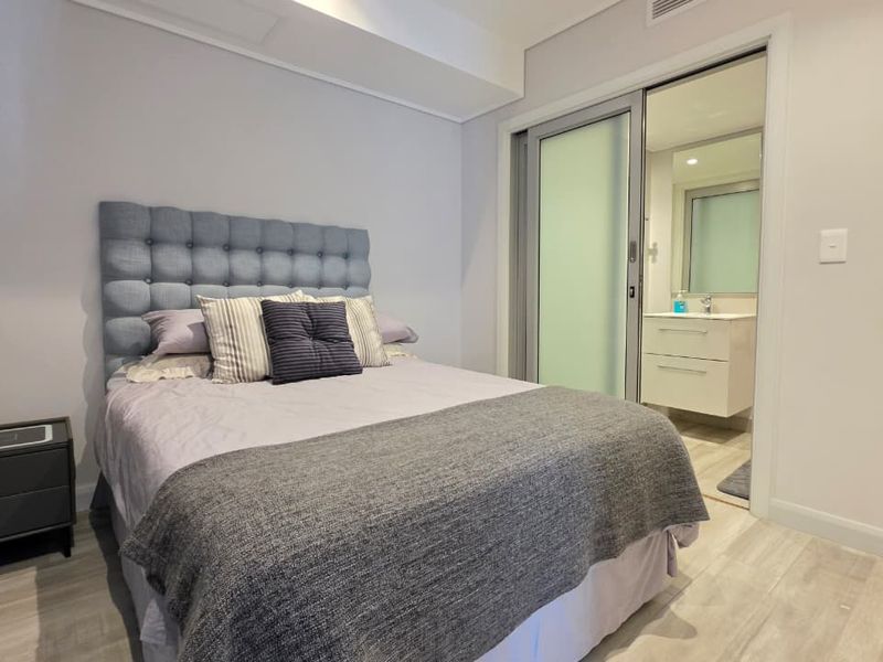 A well-maintained bedroom featuring modern laminate flooring, recessed lighting, and direct access to an en-suite bathroom through a sliding glass door.