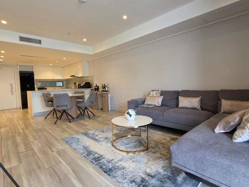Modern open-plan living and dining area featuring light laminate flooring, recessed lighting, and a sleek kitchen with integrated cabinetry.