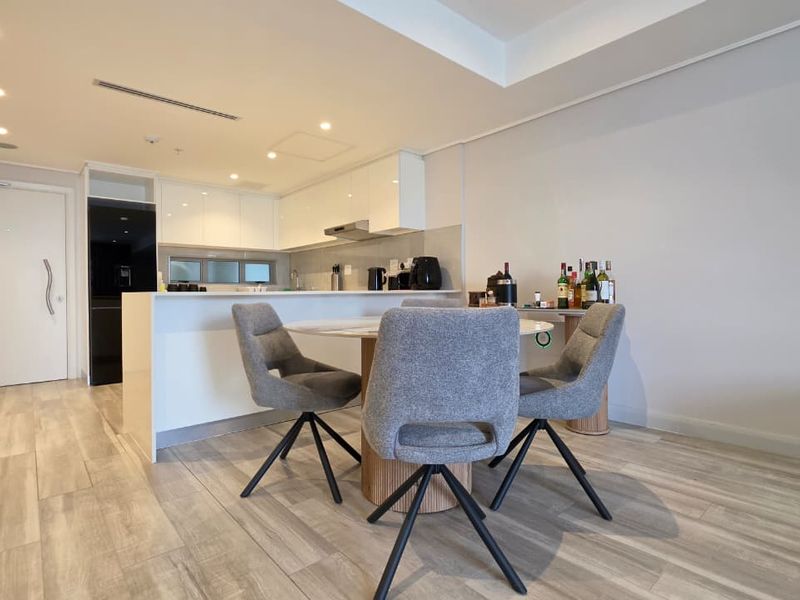 Modern open-plan living area featuring a sleek kitchen with built-in cabinetry, recessed lighting, and light-toned laminate flooring throughout.